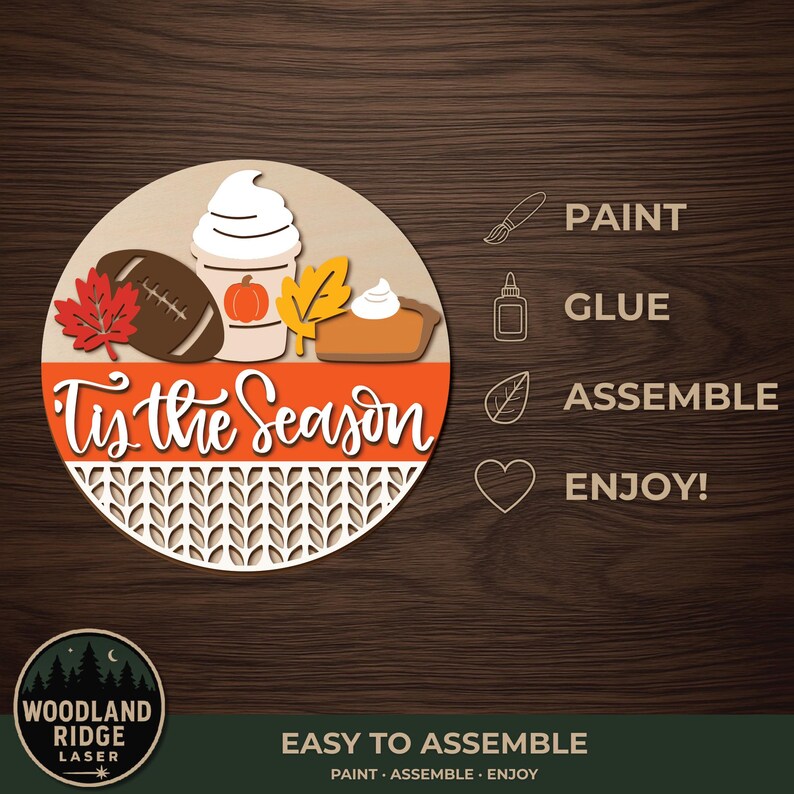 May include: A circular wooden craft kit featuring a football, a pumpkin spice latte, a maple leaf, and a slice of pumpkin pie. The text 'Tis the Season' is written in white script over an orange band, with a knit-patterned base. Includes icons for paint, glue, assemble, and enjoy.