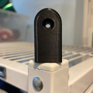 May include: A black plastic shelf support bracket with a hole in the centre. The bracket is attached to a white metal shelf.