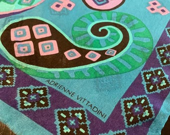May include: A close-up of a teal scarf with a colorful, abstract design. The scarf features a large, swirling pattern in green and black, with pink and blue accents. The border is a deep purple with geometric shapes. The text "ADRIENNE VITTADINI" is visible.