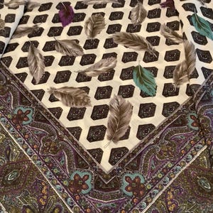May include: A white fabric scarf with a paisley border and a repeating pattern of brown feathers on a white background.