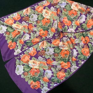 May include: A purple silk scarf with a floral pattern of orange and white roses. The scarf is folded in half and has a fringed edge.
