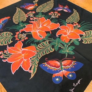 Puede incluir: Un pa&ntilde;uelo cuadrado negro con un patr&oacute;n floral central de grandes lirios naranjas, hojas verdes similares a helechos y varias mariposas coloridas en tonos azul, naranja y rojo. La firma Jim Thompson est&aacute; impresa en blanco en la esquina.