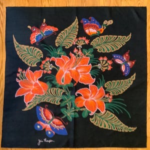 Puede incluir: Un pa&ntilde;uelo cuadrado negro con un arreglo central de flores de lirio de color naranja brillante y hojas verdes similares a helechos. Cuatro mariposas coloridas con alas azules, naranjas y rojas se sit&uacute;an alrededor del grupo floral. La firma Jim Thompson est&aacute; impresa en blanco en la esquina inferior izquierda.