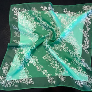 May include: A green silk scarf with a white bubble pattern. The scarf is folded in half and has a green border.