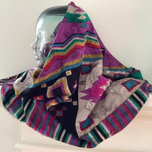 Peut inclure: Un foulard en soie coloré drapé sur une tête en verre. Le foulard présente un motif géométrique avec des accents violets, noirs et turquoise. Les bords sont finis avec une bordure à franges, ajoutant de la texture et de l'intérêt visuel.