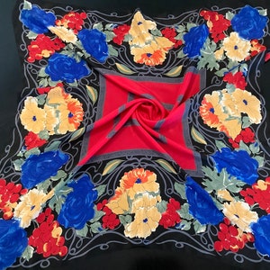 May include: A black silk scarf with a floral pattern. The pattern features red, yellow, and blue flowers on a black background. The scarf has a red and black centre.