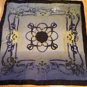 May include: A square silk scarf with a repeating equestrian-themed design. The scarf features a central dark navy blue medallion surrounded by intricate navy blue and gold patterns. The border is a dark navy blue.