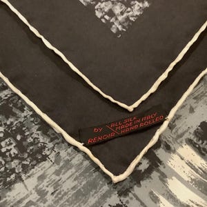 May include: A black silk scarf with a white border and a red label that reads "All Silk Made in Italy by Renoir Hand Rolled". The scarf has a gray and white abstract pattern.