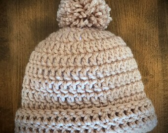 Könnte beinhalten: Eine beige gestrickte Mütze mit einem flauschigen Bommel oben.
