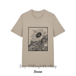 K&ouml;nnte beinhalten: Steinfarbenes T-Shirt mit einer Schwarz-Wei&szlig;-Sonnenblumenillustration in einem rechteckigen Rahmen. Das Shirt hat kurze &Auml;rmel und einen Rundhalsausschnitt. Der Etsy-Shop-Name und das Wort "Stone" sind unten aufgedruckt.
