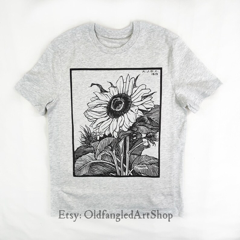 K&ouml;nnte beinhalten: Hellgraues T-Shirt mit einer Schwarz-Wei&szlig;-Illustration einer Sonnenblume. Das Kunstwerk ist in einem schwarzen Rechteck gerahmt und enth&auml;lt den Text "A.J.D.C. 1919". Der Etsy-Shop-Name "OldfangledArtShop" befindet sich unten.