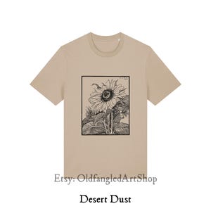 K&ouml;nnte beinhalten: Ein beiges T-Shirt mit einer Schwarz-Wei&szlig;-Illustration einer Sonnenblume in einem rechteckigen Rahmen. Der Text "Desert Dust" ist darunter gedruckt. Der Etsy-Shop-Name "OldfangledArtShop" ist ebenfalls sichtbar.
