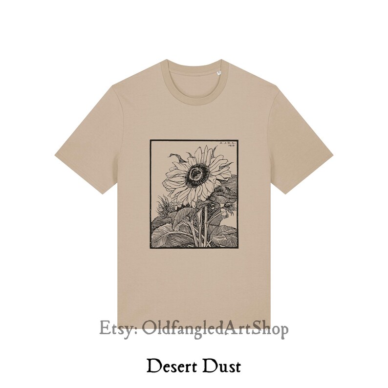 K&ouml;nnte beinhalten: Ein beiges T-Shirt mit einer Schwarz-Wei&szlig;-Illustration einer Sonnenblume in einem rechteckigen Rahmen. Der Text "Desert Dust" ist darunter gedruckt. Der Etsy-Shop-Name "OldfangledArtShop" ist ebenfalls sichtbar.