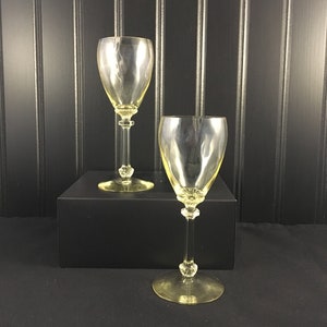 May include: Two clear yellow glass wine glasses with a stemmed base and a round bowl. The glasses are on a black surface.