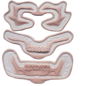 Puede incluir: Un conjunto de cuatro moldes dentales blancos con dientes rosados. Los moldes tienen forma de boca y muestran los dientes superiores e inferiores.