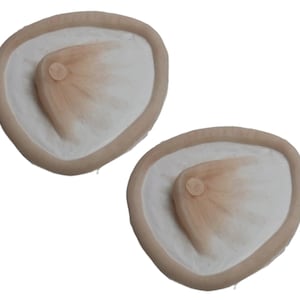 May include: Two beige silicone breast forms with a raised nipple in the center.