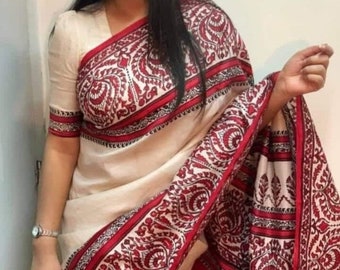 May include: Cream-colored saree with a red and white paisley pattern. The saree features a red border and matching sleeves. The design includes intricate floral and scrollwork motifs, creating a traditional and elegant look.