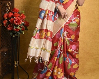 May include: A red and cream silk saree with a floral print. The saree has a cream coloured border with a floral design. The saree is draped over a person's body.