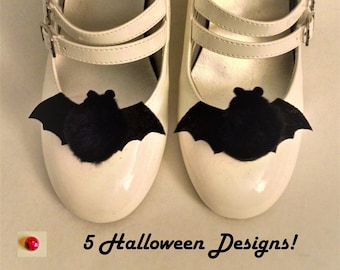 May include: A pair of white shoes with black bat embellishments. The shoes have a double strap design and a rounded toe. The text "5 Halloween Designs!" is visible below the shoes.