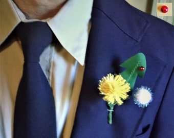 以下が含まれることがあります： 白いシャツと濃い青色のネクタイをつけた濃い青色のスーツジャケット。ジャケットには、黄色の花、緑の木、白いボールがラペルにピンで留められています。