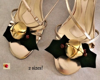 May include: A pair of gold sandals with black and red holly and gold bell embellishments. The sandals are labeled "HANDOLINO" on the insole. The text "2 sizes!" is written below the sandals.