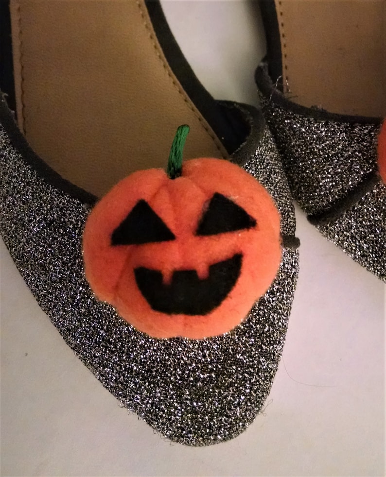 Pode incluir: Um par de sapatos de glitter prata com uma aplica&ccedil;&atilde;o de ab&oacute;bora laranja peluda. A ab&oacute;bora tem um caule, olhos, nariz e boca pretos.
