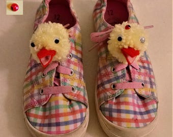 May include: A pair of pink and multi-colored plaid children's sneakers with yellow chick pom-poms on the toes. The sneakers are size 12.