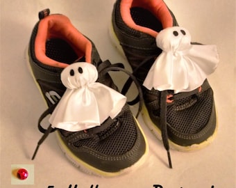 May include: Two black sneakers with white laces and a bright yellow trim. Each shoe has a white ghost with a black face attached to the top. The text "5 Halloween Designs!" is at the bottom of the image.