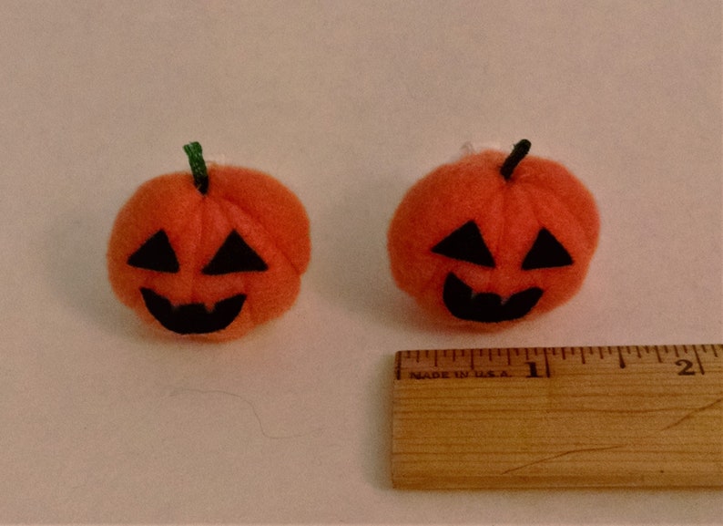 Pode incluir: Duas pequenas ab&oacute;boras de feltro laranja com rostos de feltro preto. As ab&oacute;boras t&ecirc;m um di&acirc;metro de aproximadamente 2,5 cm.