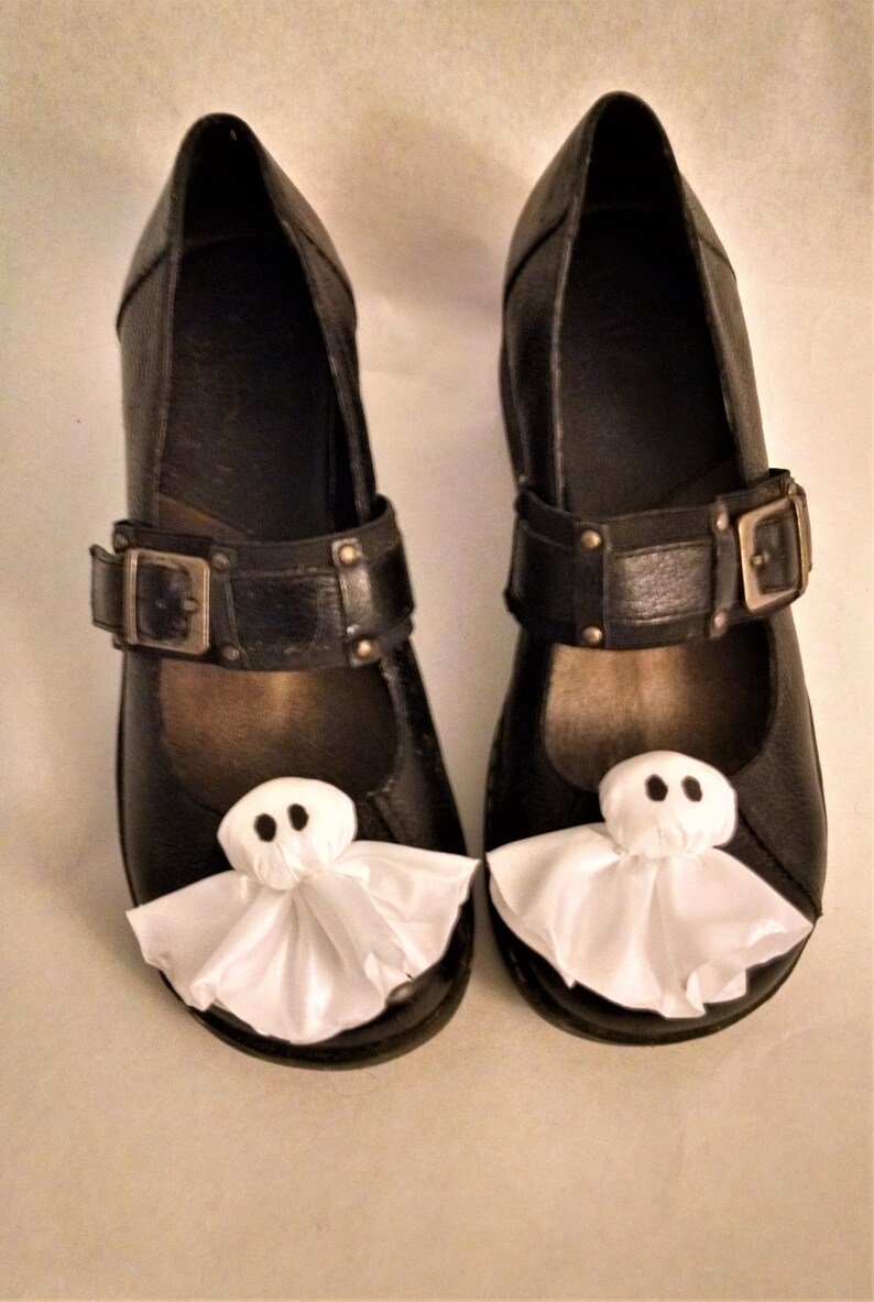 Pode incluir: Um par de sapatos de couro preto com decora&ccedil;&otilde;es de fantasmas brancos nos dedos. Os sapatos t&ecirc;m uma fivela e uma ponta pontiaguda.