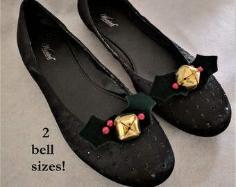 May include: A pair of black ballet flats with a festive touch. Each flat features a green holly leaf with red berries and a gold bell. The shoes have a subtle sparkle and the text "Wanted" is visible on the inside of the shoes.