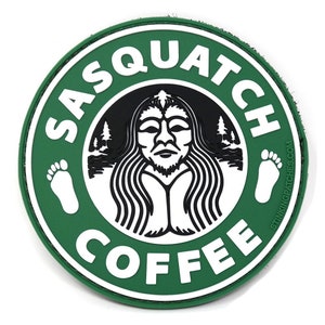 May include: A green and white circular patch with the text "Sasquatch Coffee" and a black and white image of a Sasquatch with a beard and long hair. The image is surrounded by a circle of trees and the text "StinkingPatches.com" is on the right side of the patch.