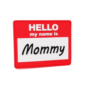 Può includere: Un cartellino rosso con testo bianco che recita "HELLO my name is Mommy" e un indirizzo di sito web in basso.