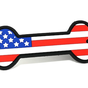 Puede incluir: Un parche con forma de hueso de perro rojo, blanco y azul con un diseño de bandera estadounidense.