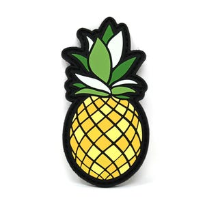 Può includere: Un ananas giallo con una cima di foglie verdi e bianche. L'ananas è contornato di nero e ha un motivo testurizzato.
