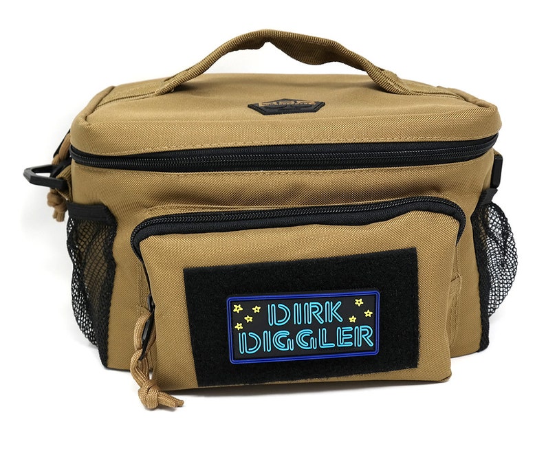 May include: A tan canvas lunch bag with a black zipper and a black mesh pocket on the side. The bag has a black patch with the text "DIRK DIGGLER" in blue and yellow.