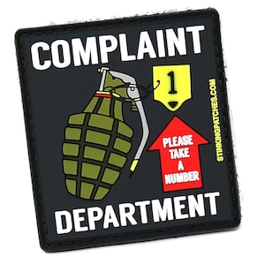 Könnte beinhalten: Ein schwarz-weißes Patch mit dem Text "COMPLAINT DEPARTMENT" und einem Cartoon-Bild einer Granate mit einem roten Pfeil, der nach oben zeigt, mit dem Text "PLEASE TAKE A NUMBER" und einem gelben Schild mit der Nummer "1", das an der Granate hängt.