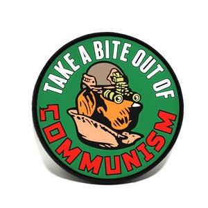Puede incluir: Un parche redondo verde y rojo con el texto "Take a Bite Out of Communism" en blanco. Una ilustración de dibujos animados de un perro con una máscara de gas está en el centro del parche.