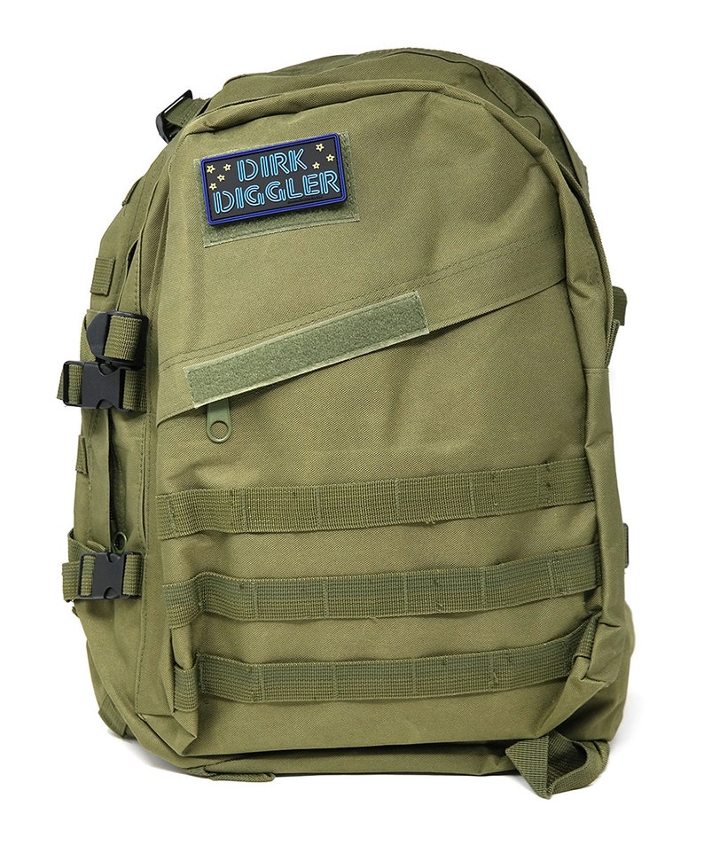 May include: A green military-style backpack with multiple straps and buckles. A patch with the text "DIRK DIGGLER" in blue neon lettering is attached to the front.
