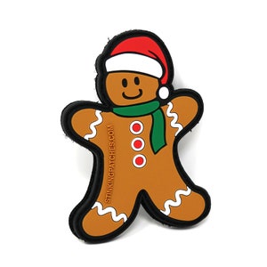 May include: A gingerbread man patch with a red Santa hat, green scarf, and three red button details. The patch has a black border and the text "STINKINGPATCHES.COM" on the side. The gingerbread man is brown with white icing details.