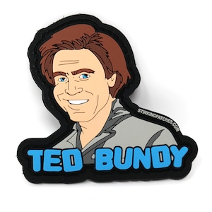 May include: A black and blue embroidered patch with a cartoon image of Ted Bundy, a serial killer, with the text "TED BUNDY" in blue.