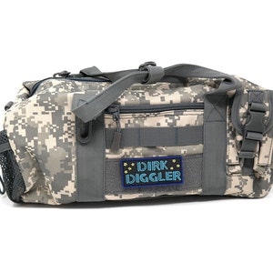 May include: A camouflage-patterned duffel bag with a gray zipper and a black patch that reads "DIRK DIGGLER" in blue and yellow lettering.