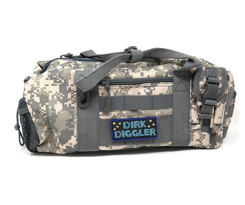 May include: A camouflage-patterned duffel bag with a gray zipper and a black patch that reads "DIRK DIGGLER" in blue and yellow lettering.