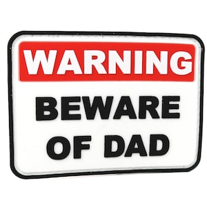 Puede incluir: Un cartel de advertencia blanco con una banda roja en la parte superior que dice "WARNING" en letras blancas. El cartel dice "BEWARE OF DAD" en letras negras.