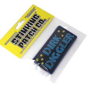 May include: A blue and yellow iron-on patch with the text "DIRK DIGGLER" in a neon blue font. The patch is packaged in a clear plastic bag with a yellow header that reads "STINKING PATCH CO."