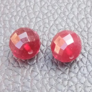 May include: Two red faceted glass beads, each with a slightly different shape and size.