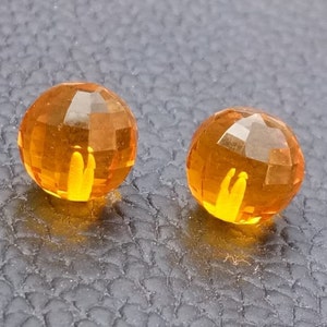 Peut inclure: Deux perles rondes en verre orange facettées. Les perles sont lisses et brillantes.