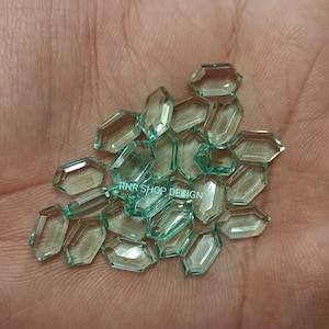 May include: A pile of light green faceted gemstones in an octagon shape. The gemstones are translucent and have a slight sparkle.