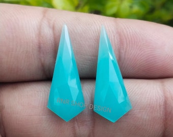 May include: Two turquoise blue gemstone pendants with a pointed, faceted design. The pendants are translucent and have a gradient of color from light to dark blue.