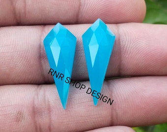 May include: Two turquoise blue gemstone cabochons in a pointed, faceted shape. The stones are approximately 1 inch long and have a smooth, polished finish.